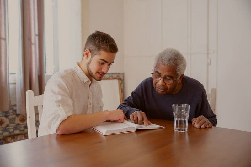 A support worker with a lanyard listening to an older woman on a sofa during a home visit